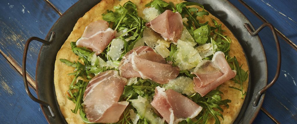 Pizza with pork bresaola, rocket salad and Parmesan flakes