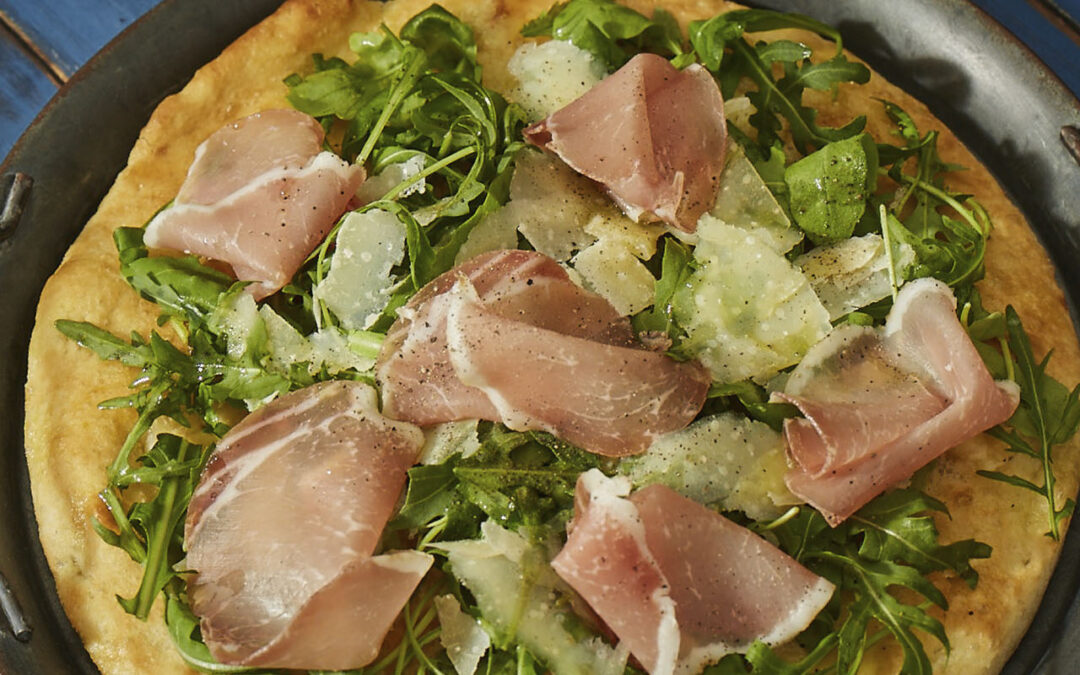 Pizza with pork bresaola, rocket salad and Parmesan flakes